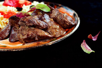 Fried chicken liver, juicy soft and tender meat with young beet leaves on a black background on the side, empty space