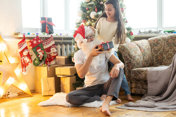 Picture of happy family celebrating New Year eve, little girl with parents enjoying winter holidays, father wearing Santa Claus costume, Christmas magic, happiness and love concept