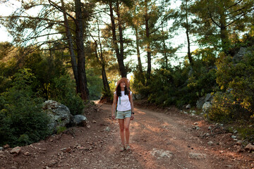 Fototapeta na wymiar a traveler girl with a backpack walks along a forest road.