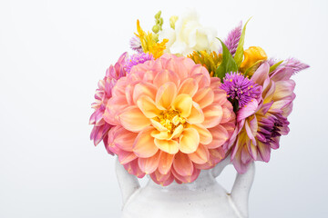 Beautiful floral arrangement, white background. Dahlia, celosia, and snapdragon flowers. Pink, yellow, white flowers. Small white jug used as the vase. Space for text.