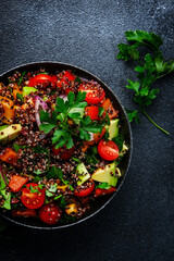 Quinoa tabbouleh salad with tomatoes, paprika, avocado, cucumbers, onion and parsley. Traditional Middle Eastern and Arabic dish. Black kitchen table background, top view