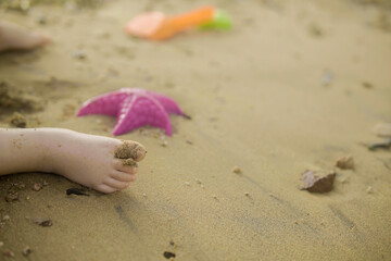child's feet on the sand on the beach next to toys