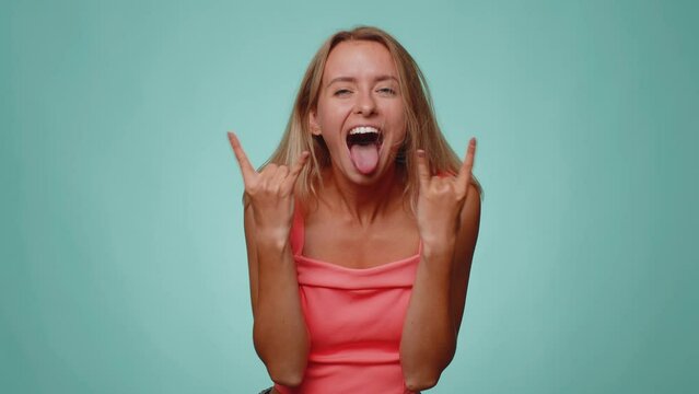 Rock n roll. Overjoyed delighted pretty woman 20s in crop top showing gesture by hands, cool sign, shouting yeah with crazy expression, dancing, emotionally rejoicing in success win alone on blue wall