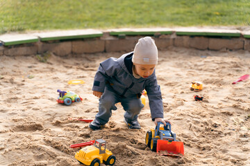 Child playing with toys in sandbox. Little boy having fun on playground in sandpit. Outdoor...