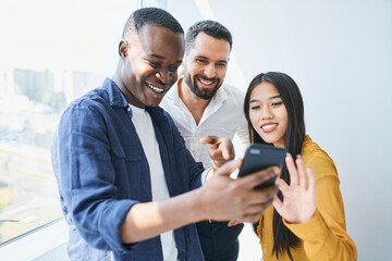 Happy coworkers looking at phone in office. Students share smartphone at university