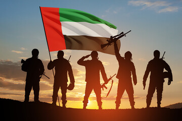 Silhouettes of soldiers with the flag of UAE on background of the sunset or the sunrise....
