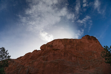 Fototapeta na wymiar Sun coming up from behind a bare rock mountain, blue sky and clouds, Colorado American west, horizontal aspect