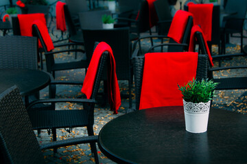 View of empty terrace of open air cafe with black tables and chairs with red blankets.