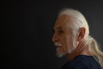 Low key studio  portrait of beautiful old man - rocker fan - looking over his shoulder at the...