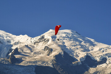 A red paraglider flying in front of Mont Blanc mountain in the French Alps in summer, Chamonix-Mont-Blanc, Haute-Savoie, France