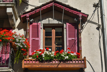 Detail of the window of a typical alpine house with flowering geraniums on the sill in summer,...