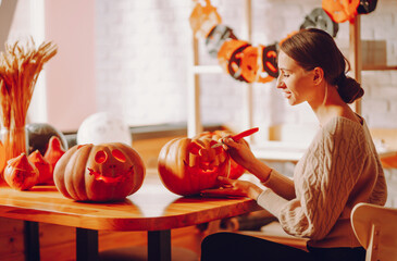 Halloween, decoration and holiday concept - close up of woman with knife carving pumpkin.