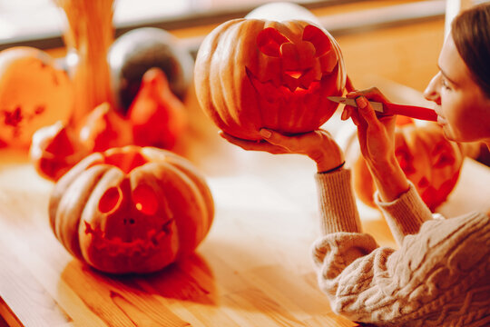 Halloween, decoration and holiday concept - close up of woman with knife carving pumpkin.