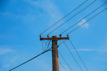 Electric pole power lines outgoing electric wires againts on cloud blue sky.