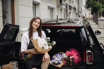 A woman florist puts flowers in the trunk of a car. Flower delivery concept.