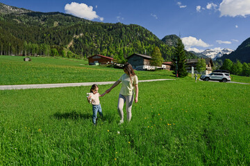 Mother holding hands daughter and walking in alpine meadow at Untertauern, Austria.