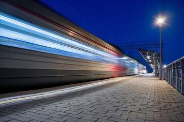Evening arrival of the train on an empty platform. Photo taken with a shutter speed. Rays of light. Blur. Evening railway station.