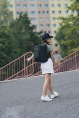 A girl with braids in a black hat with a backpack returns or goes to school on the street. 