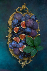 Fresh fruits figs, grapes and plums on a vintage dish on a blue background. Top view