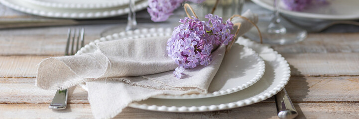 Beautiful table decor for a wedding dinner with a spring blooming lilac flowers. Celebration of a special event. Fancy white plates, and wineglasses. Countryside style. Banner