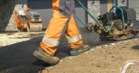 Rear view of worker using vibration compactor for smoothing asphalt surface