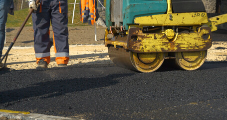 Working with asphalt roller for compacting and smoothing surface at driveway