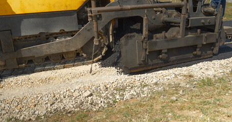 CLOSE UP: Asphalt paver machine dumping and spreading blacktop over crushed rock