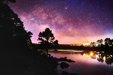 lake at night with milky way in the sky, dark sky with million of stars and forest around, arareco...