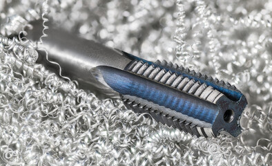 Spiral point straight fluted tap in metal swarf heap with white bokeh. Beautiful steel tapping tool...