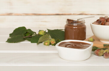 Hazelnut cream with nuts and green leaves on wooden table