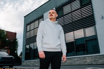 City portrait of handsome guy with mustache and beard wearing gray blank hoodie with space for your logo or design. Mockup for print