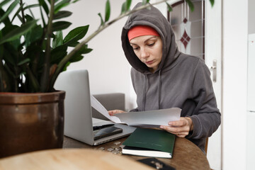 Young woman with hat and hoodie in cold home cheking papers and bills. Energy crisis in winter