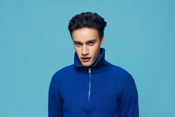 a handsome, pleasant man stands in a blue zip-up sweater smiling pleasantly at the camera. Studio photo on a light blue background with an empty space for inserting an advertising layout