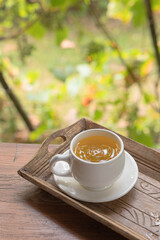 green herbal tea in a white cup with a saucer on a wooden table in a green autumn garden on a sunny day