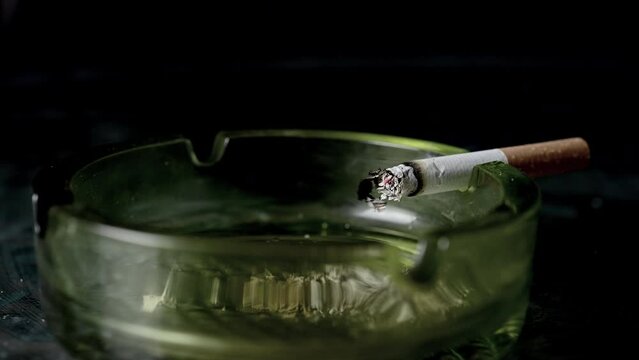 Lit cigarette burning in ashtray close up.