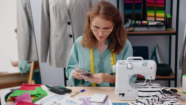 Young beautiful hispanic woman tailor counting dollars at tailor shop