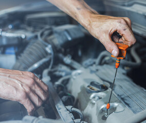 A male mechanic checks the oil level in the car engine in close-up. The mechanic holds a dipstick...
