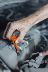 A male mechanic checks the oil level in the car engine in close-up. The mechanic holds a dipstick...