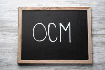 Small blackboard with abbreviation OCM (Organizational Change Management) on white wooden background, top view