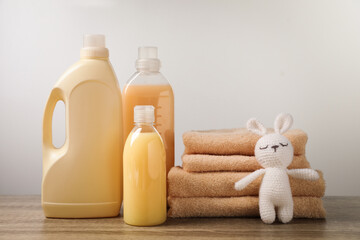 Bottles of laundry detergents, stacked fresh towels and knitted toy rabbit on table against white...