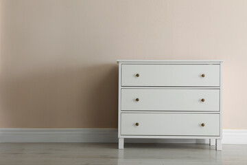 White chest of drawers near beige wall. Space for text