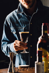 man holding an espresso martini cocktail behind the bottles in a bar