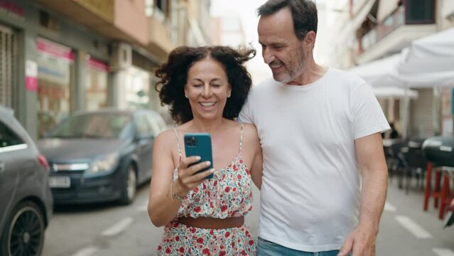 Man and woman couple hugging each other using smartphone walking at street