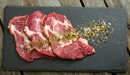 Fresh meat on slate black board top view. Raw piece of meat with spice for cooking