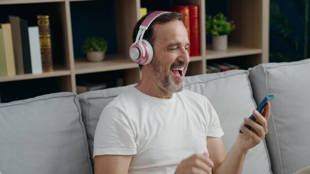 Middle age man dancing and listening to music sitting on sofa at home