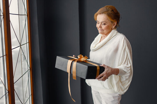 Old woman standing indoors holding a gift box