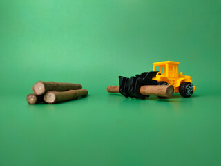 Excavator with wooden stick on green background. Conceptual image of illegal logging.