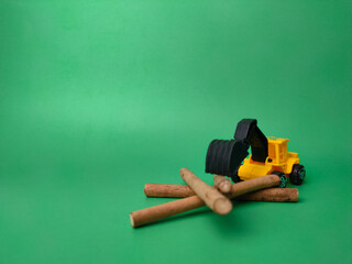 Excavator with wooden stick on green background. Conceptual image of illegal logging.