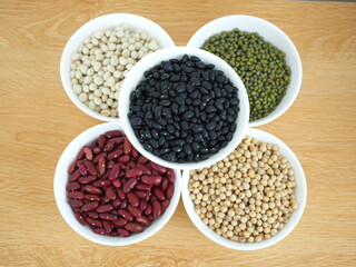 Five type of natural grains in white cup consisted of soybeans, black beans, red beans, white beans , and green beans. Top view photo, blurred.