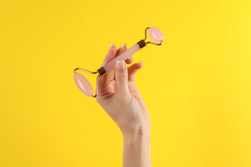 Woman's hand holds a massage jade facial roller on a yellow background. Anti-aging therapy